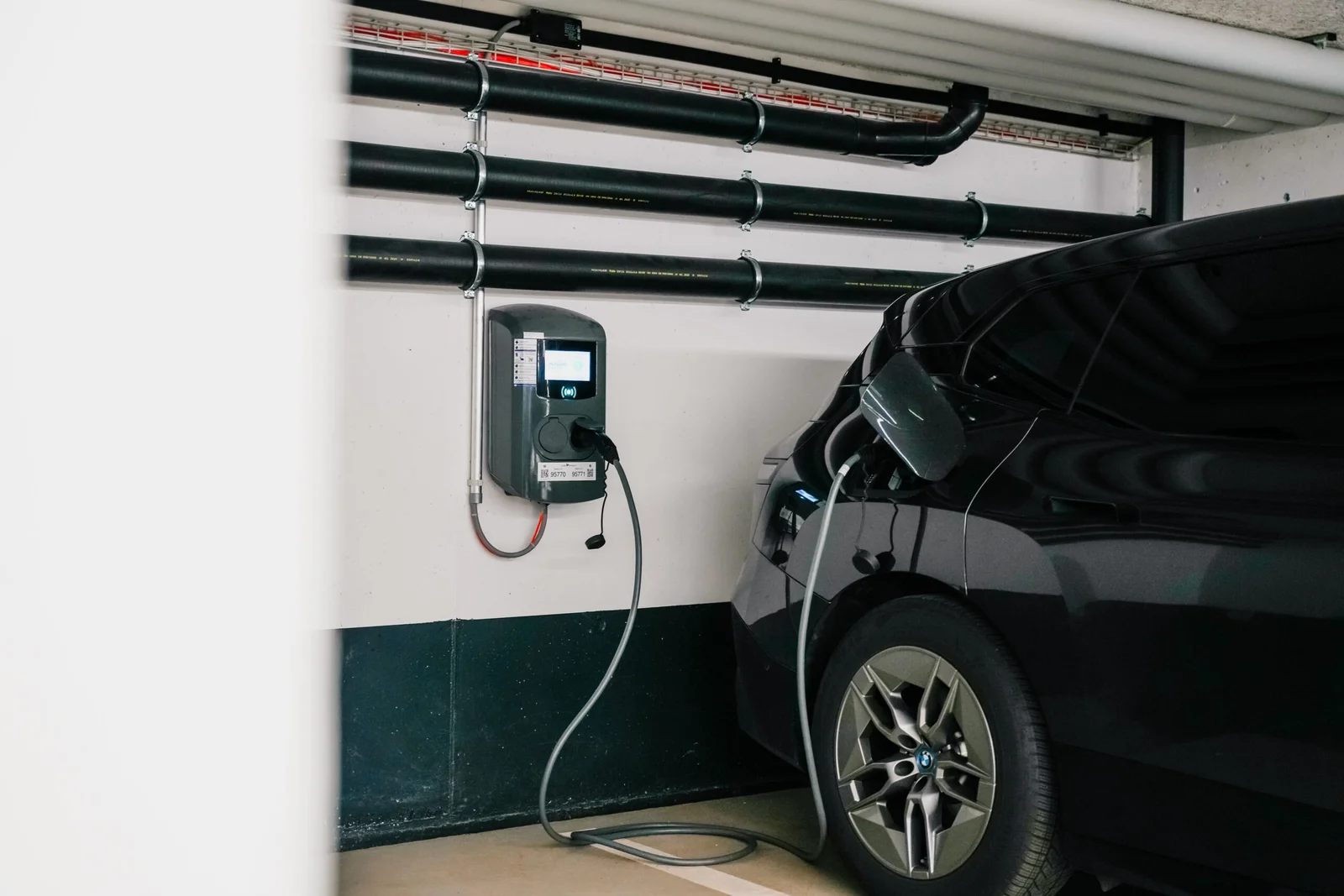 Electric vehicle charging täsch station plugged into parked car inside garage